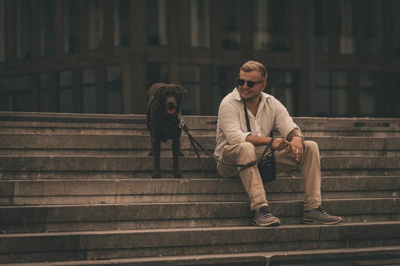 Ein Mann und sein schwarzer Hund sitzen auf einer breiten Steintreppe.