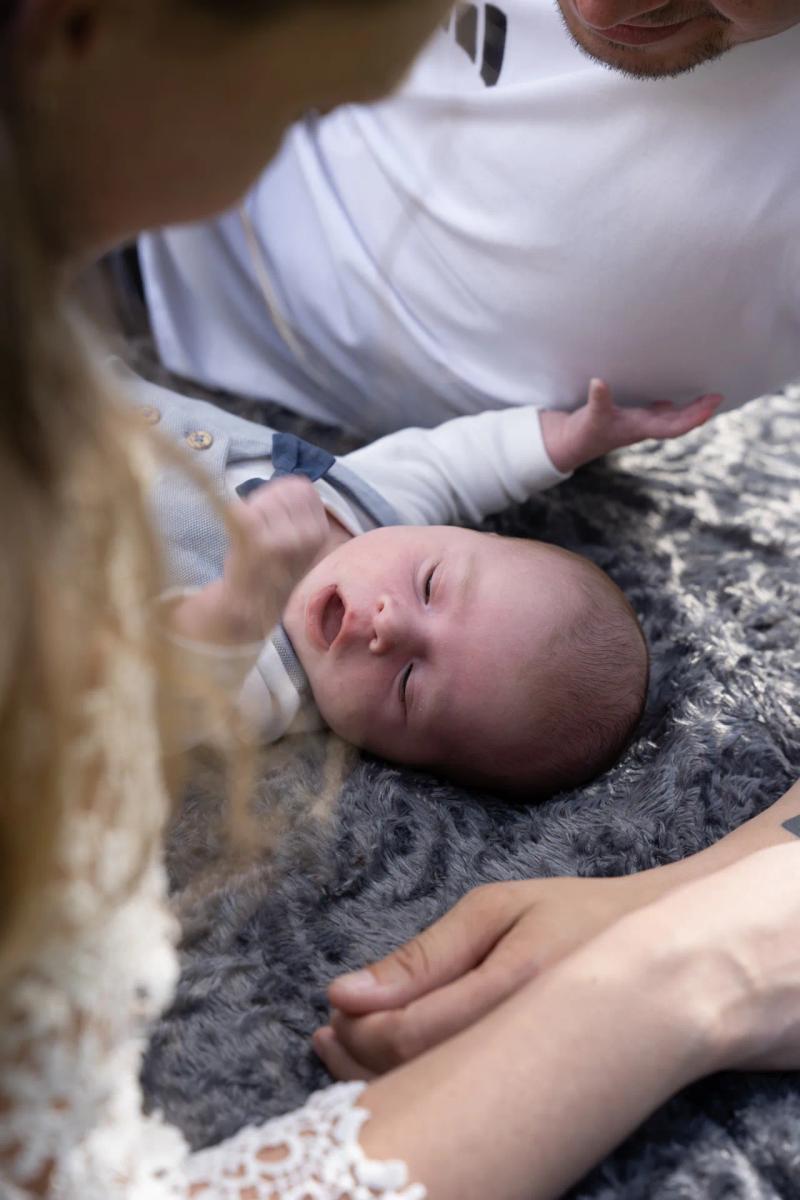 Ein Baby liegt geborgen zwischen seinen Eltern auf einer weichen Decke.