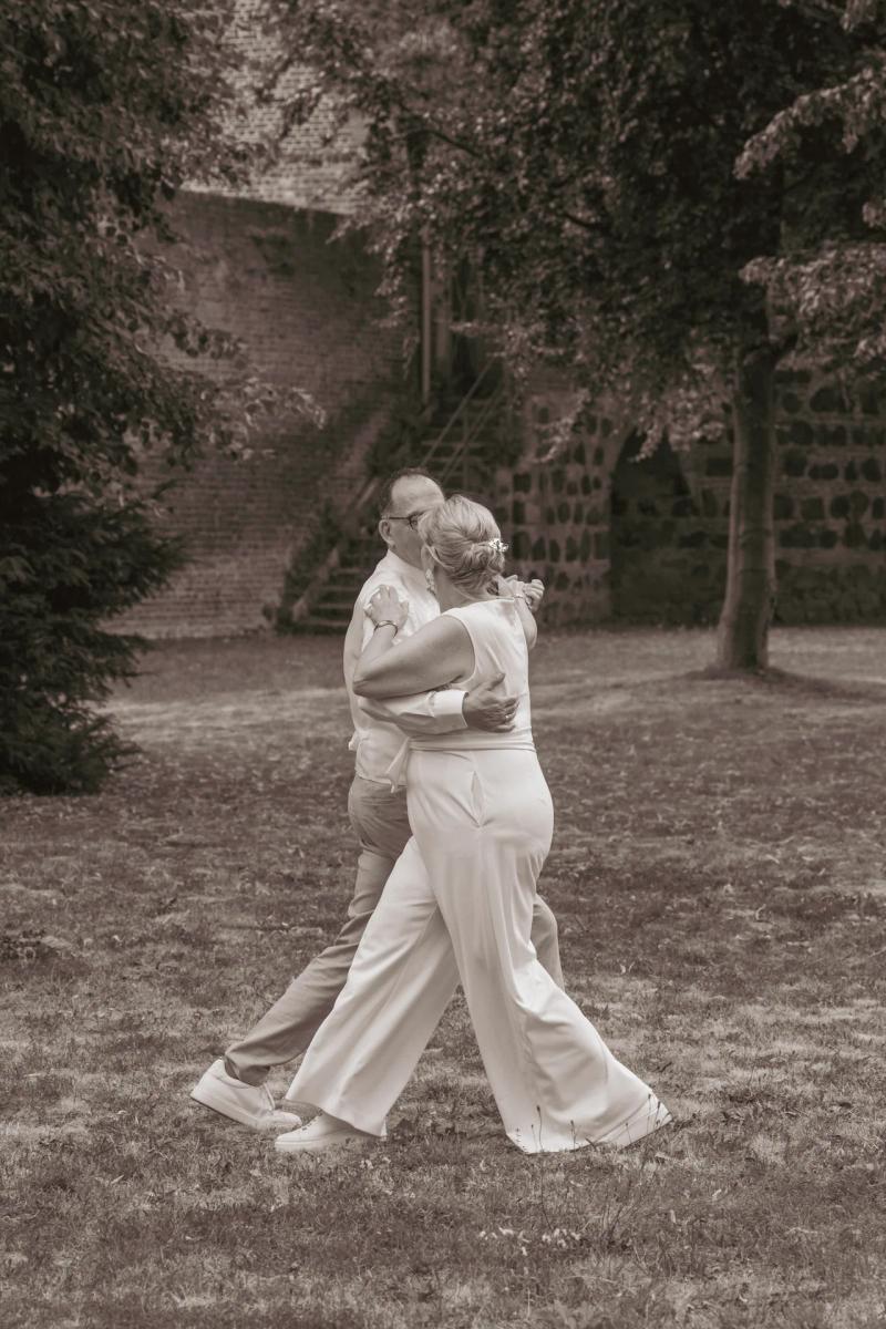 Eine Braut im langen hellen Kleid steht zwischen hohen Bäumen.