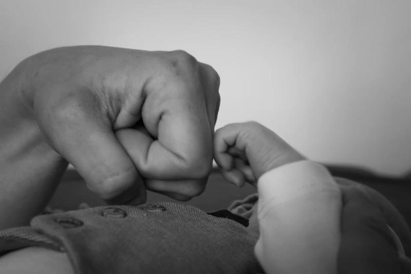 Eine kleine Babyhand berührt eine erwachsene Faust, in Schwarz-Weiß.