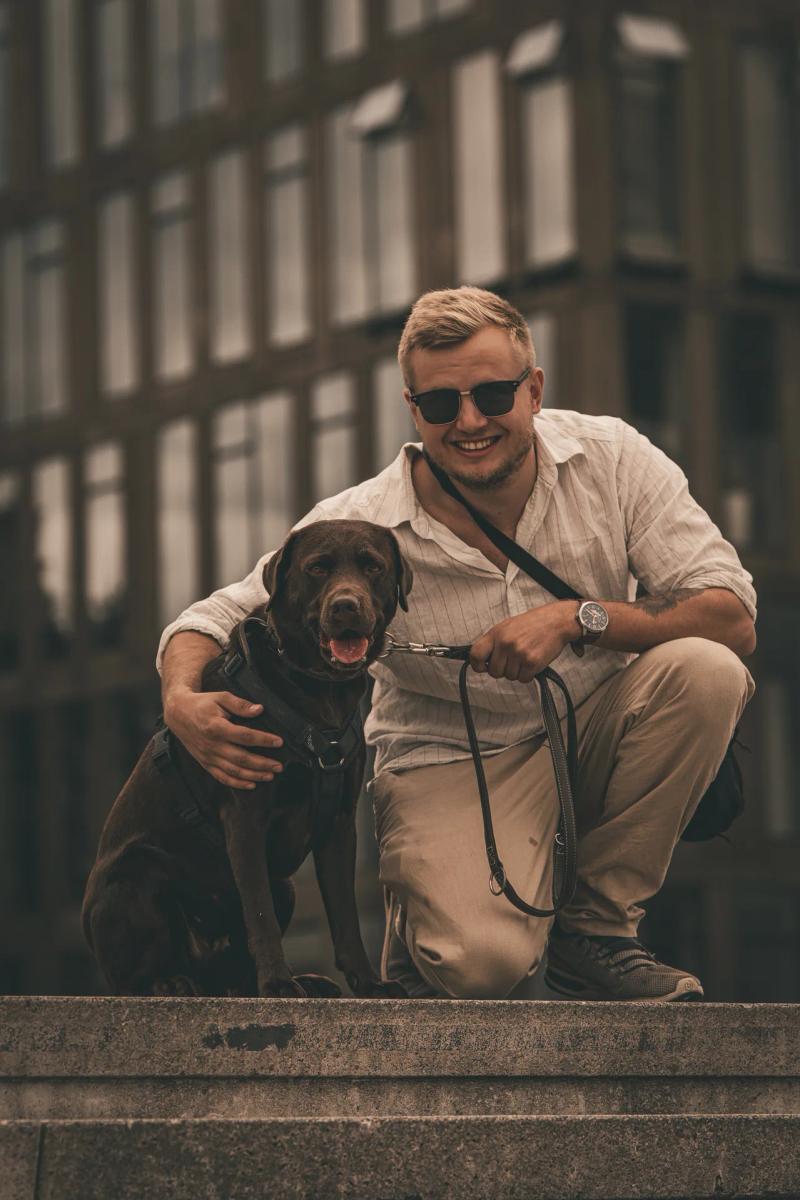 Ein Mann hockt mit seinem schwarzen Hund auf einer Treppe.