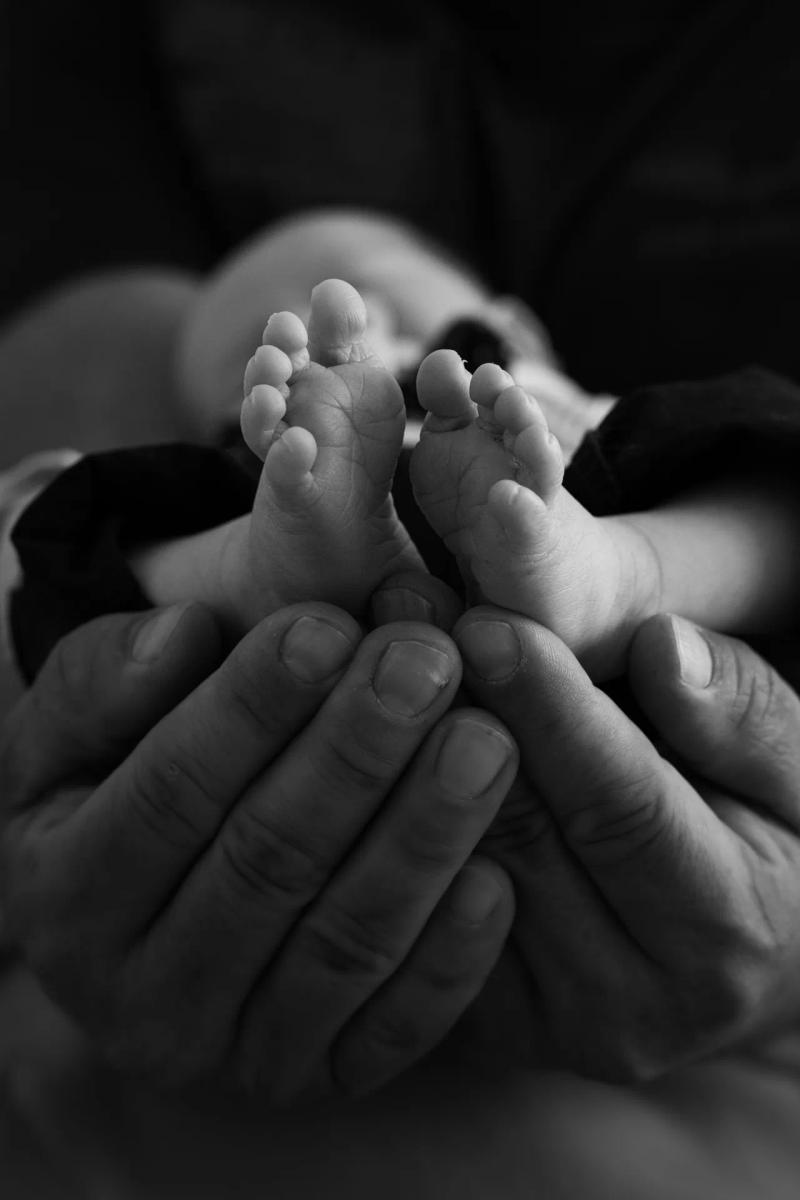 Kleine Babyfüße werden von einer erwachsenen Hand gehalten, in Schwarz-Weiß.