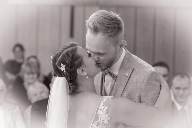 Ein Hochzeitspaar küsst sich während der Trauung, in Schwarz-Weiß.