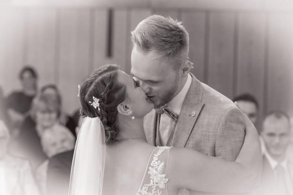 Ein Hochzeitspaar küsst sich während der Trauung, in Schwarz-Weiß.