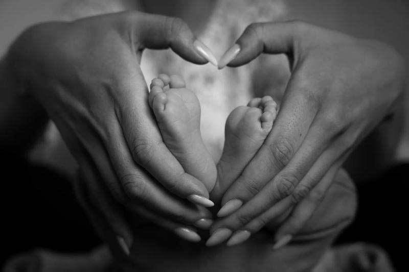 Elternhände formen ein Herz um kleine Babyfüße, in Schwarz-Weiß.