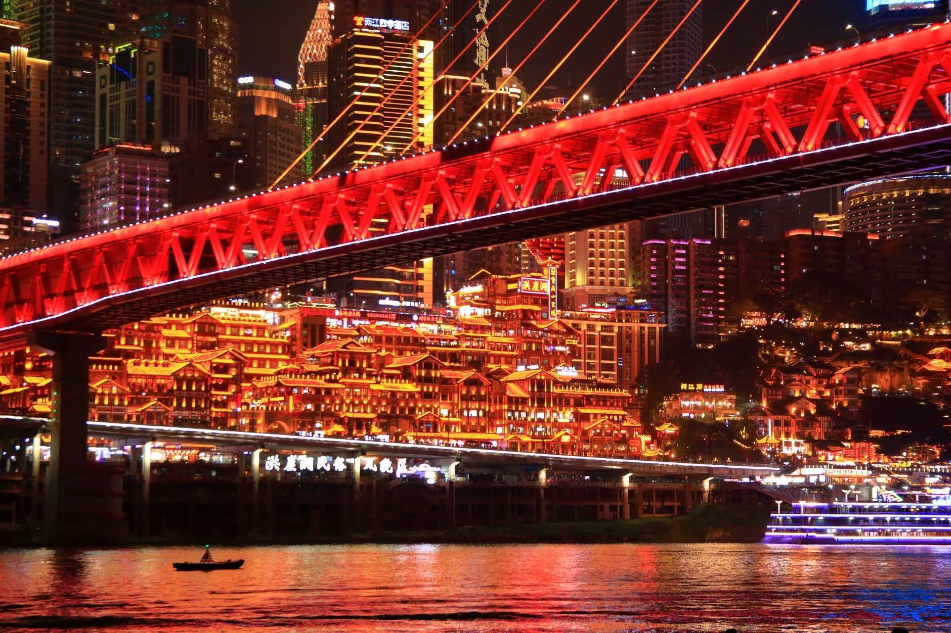 Vibrant night view of Chongqing with illuminated buildings and a striking red bridge.