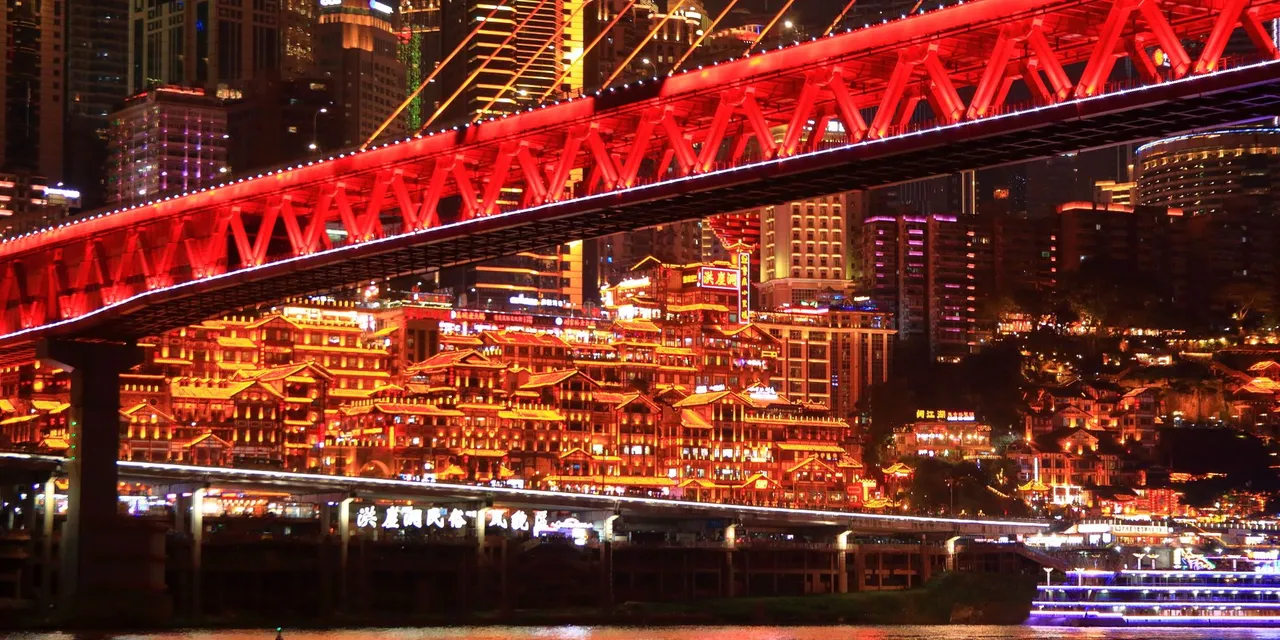 Vibrant night view of Chongqing with illuminated buildings and a striking red bridge.