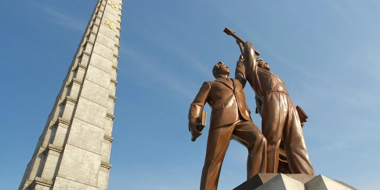 Low angle view of Juche Tower and worker statues against a clear blue sky in Pyongyang, North Korea.