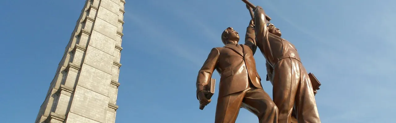 Low angle view of Juche Tower and worker statues against a clear blue sky in Pyongyang, North Korea.