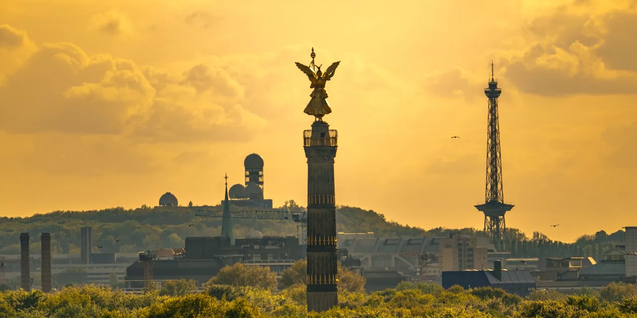 Scenic sunset view of the Victory Column in Berlin, Germany with lush green foreground and iconic city landmarks.