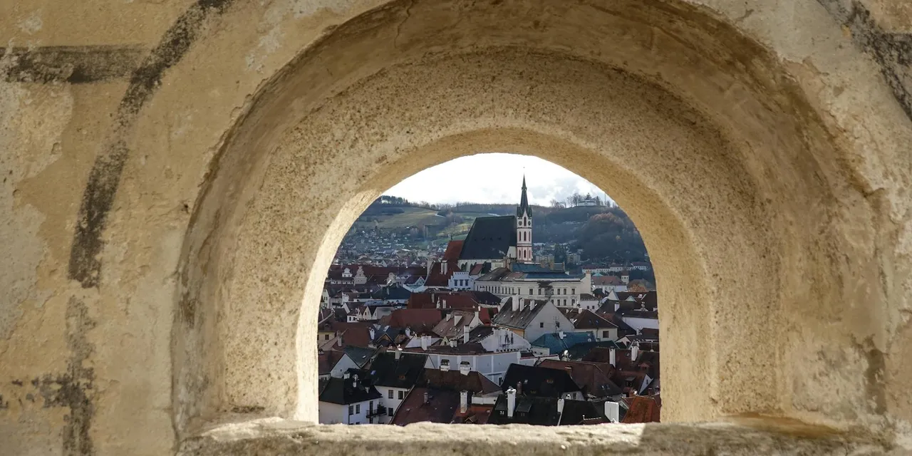 A picturesque view of Český Krumlov, Czechia, captured through an ancient archway, showcasing its historic architecture.