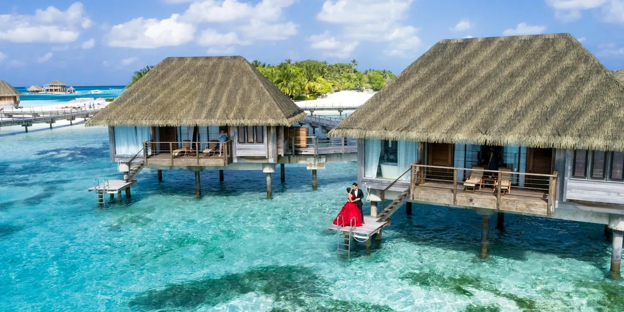 A scenic view of overwater bungalows and a couple enjoying a tropical paradise in the Maldives.
