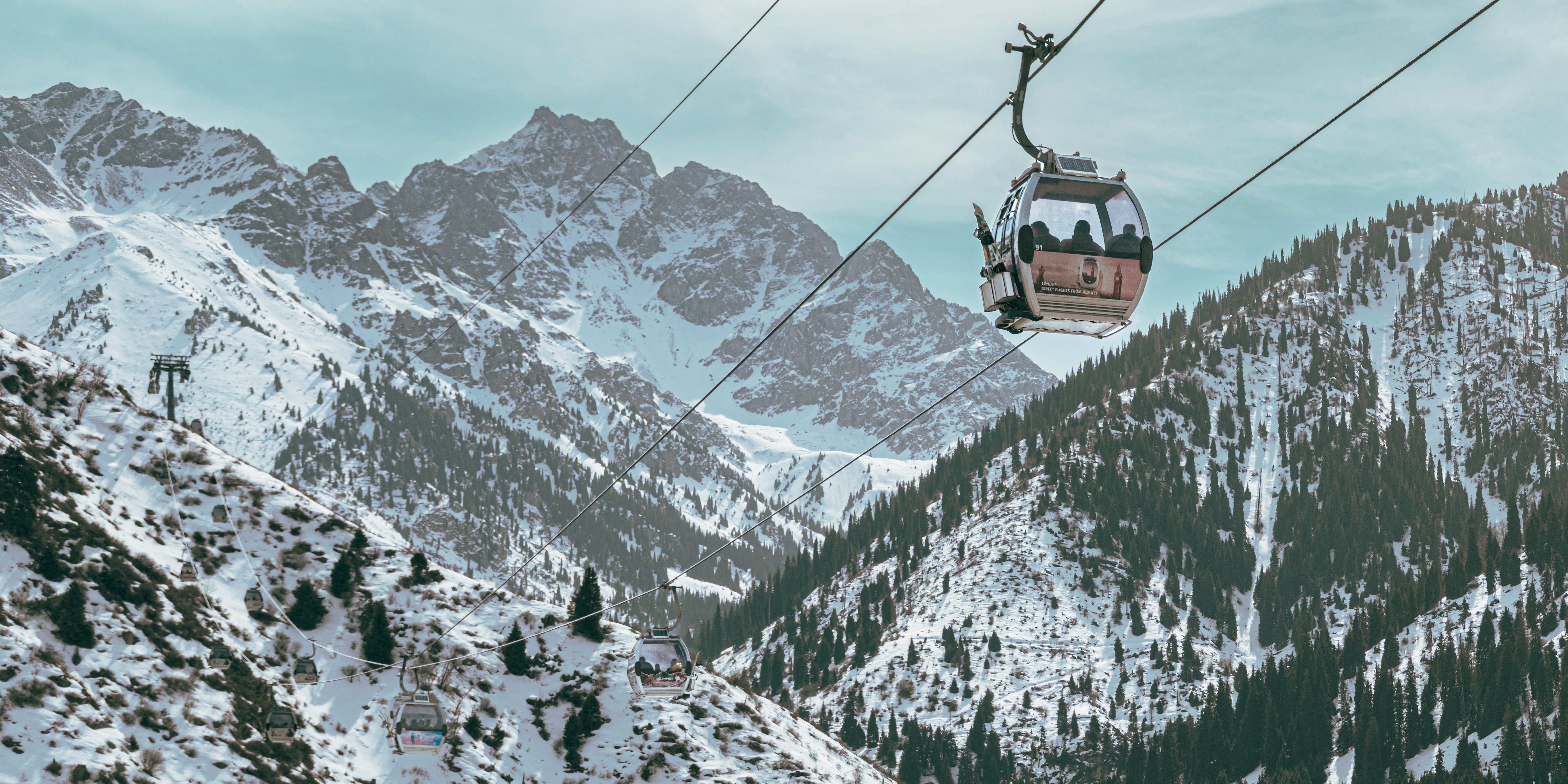 A gondola cabin rising above snow-covered mountains and conifer forest in the hills above Almaty.