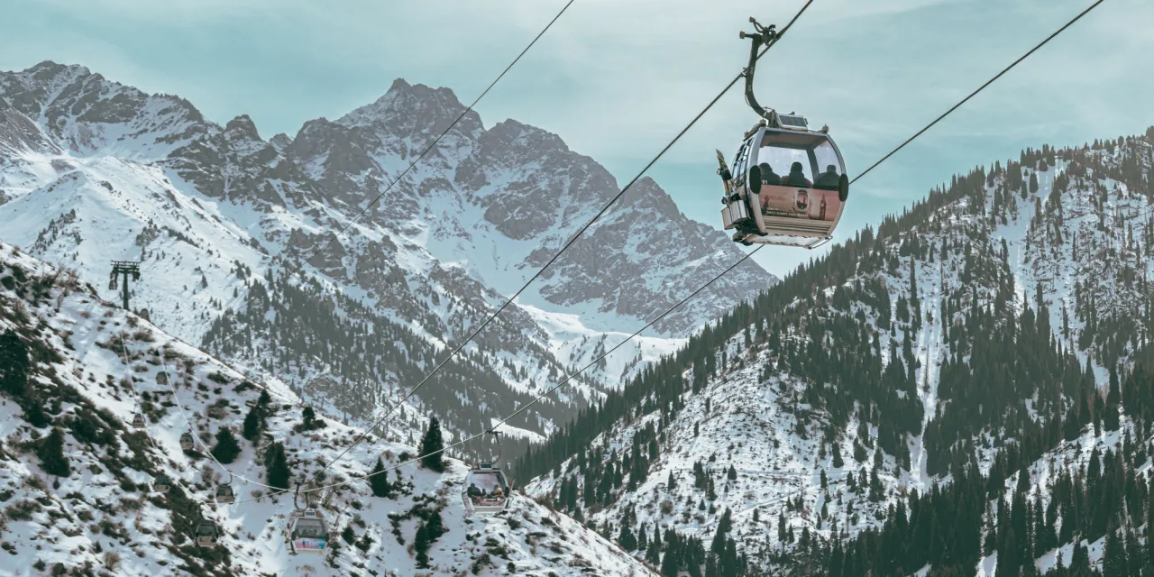A gondola cabin rising above snow-covered mountains and conifer forest in the hills above Almaty.