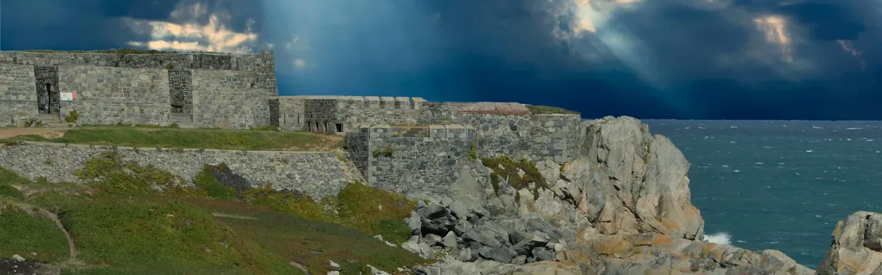 Rugged fort along Guernsey's rocky coast with dramatic clouds and sunrays breaking through.
