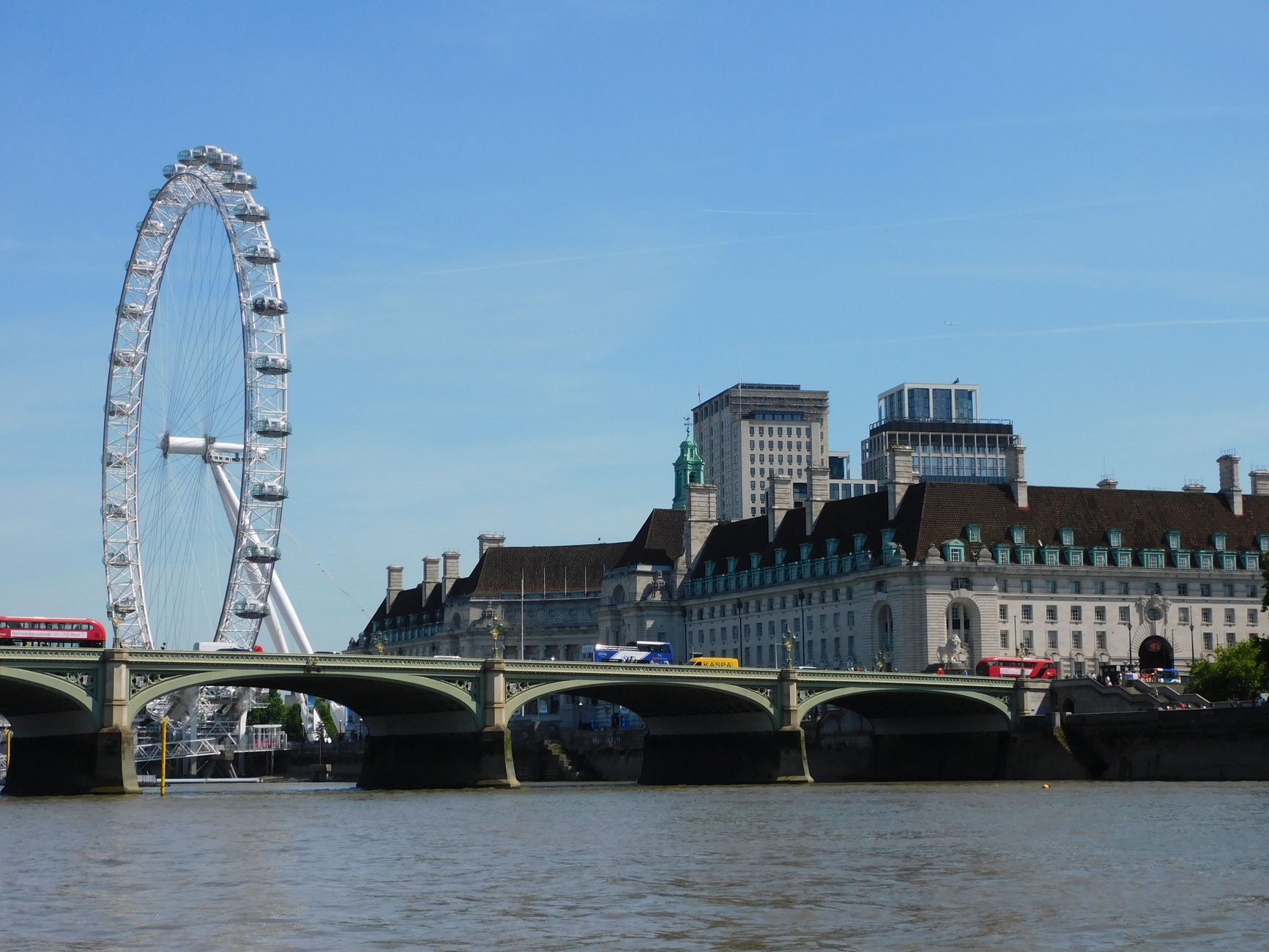 A scenic view of the London Eye and River Thames with historic architecture and clear sky.