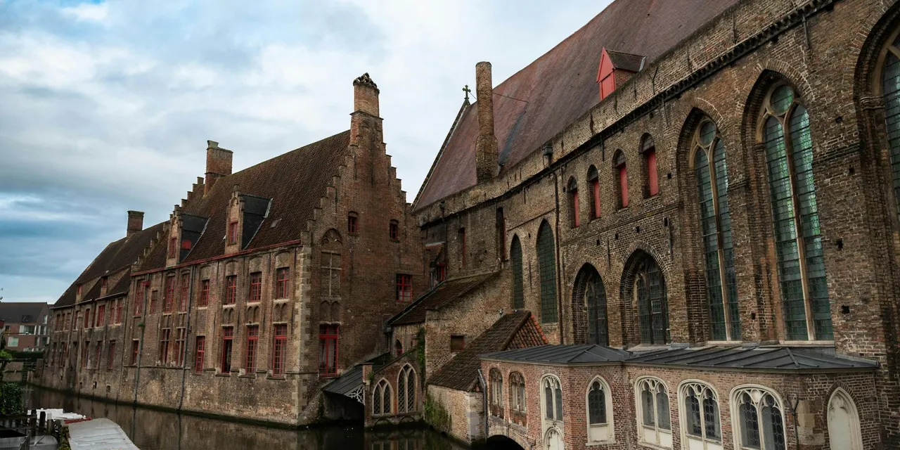 Historic brick buildings along a tranquil canal in Bruges, Belgium.
