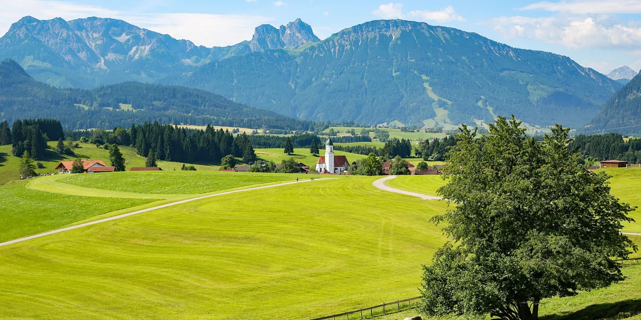 Beautiful rural landscape with lush fields, mountains, and quaint village in sunny weather.