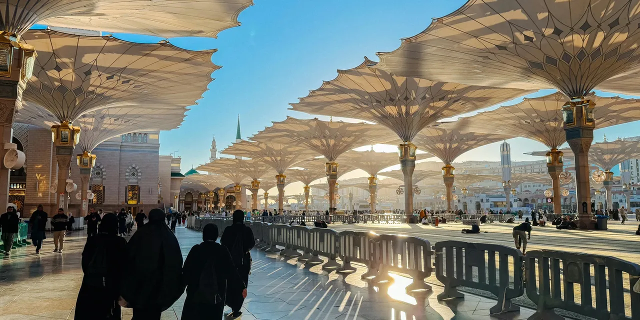 Pilgrims walking beneath the giant umbrella canopies of Al-Masjid an-Nabawi in Medina, Saudi Arabia