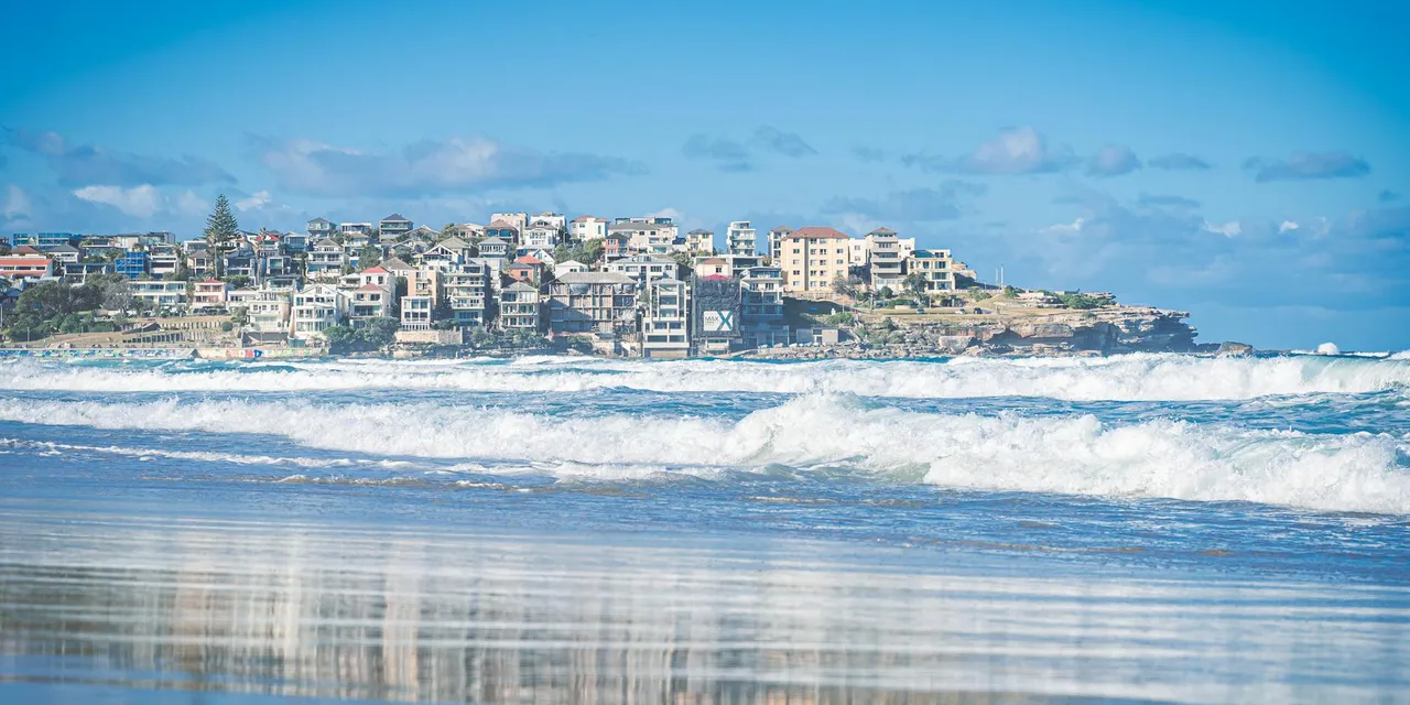 Vibrant Bondi Beach with waves lapping the shore and the urban skyline in the background under a bright blue sky.