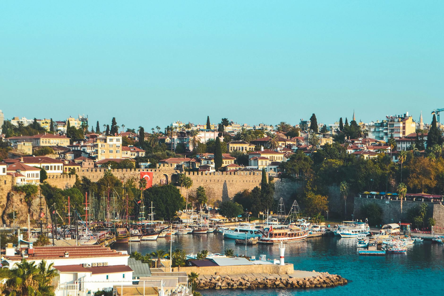 Scenery view of light blue cloudless sky above settlement and fortress wall next to ships in seaport in Turkey
