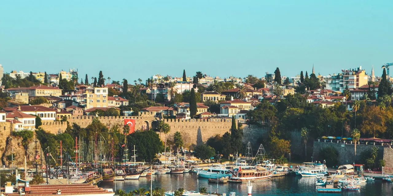 Scenery view of light blue cloudless sky above settlement and fortress wall next to ships in seaport in Turkey