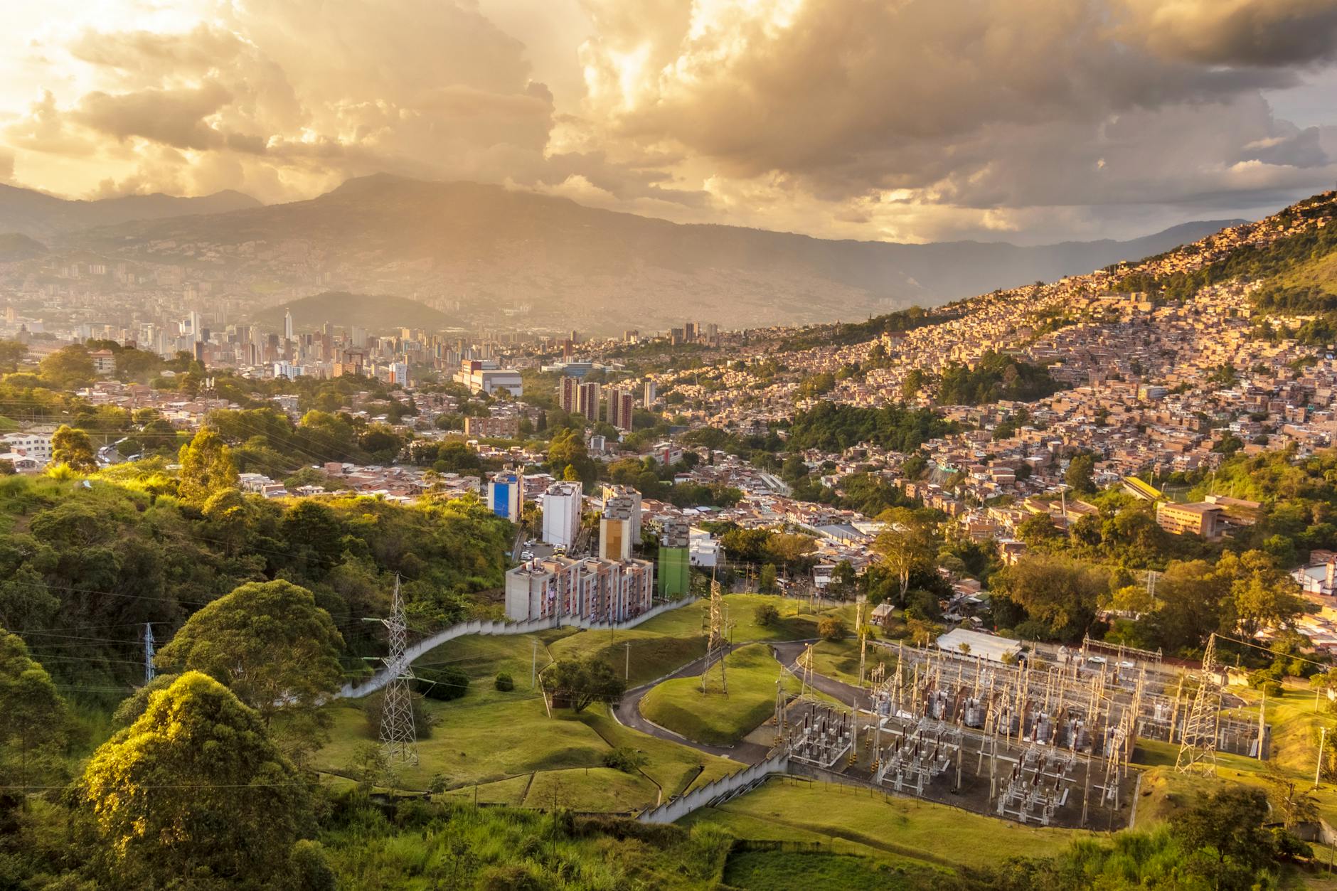 Aerial shot of Medellin, Colombia, showcasing urban sprawl and hills at sunset.