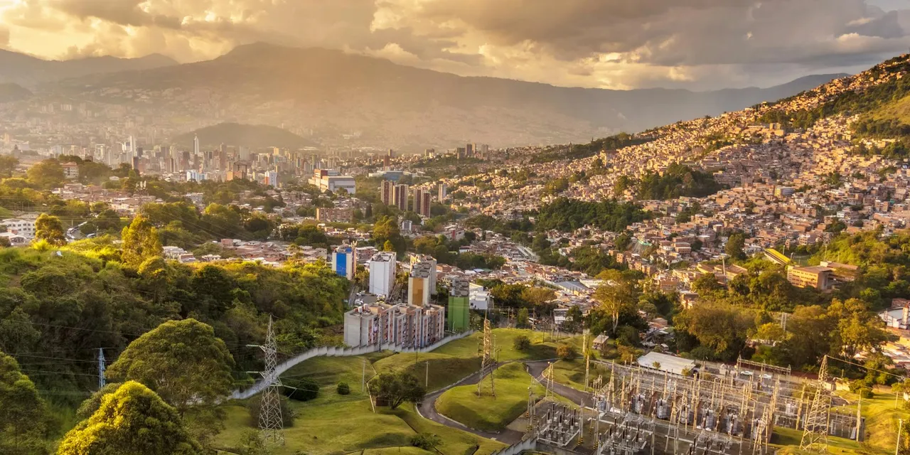 Aerial shot of Medellin, Colombia, showcasing urban sprawl and hills at sunset.