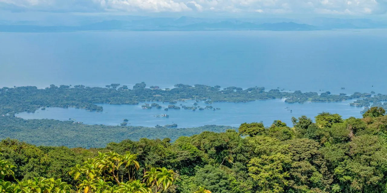 Aerial view of lush islets on Lake Nicaragua with Mombacho Volcano in the distance, captured on a sunny day.