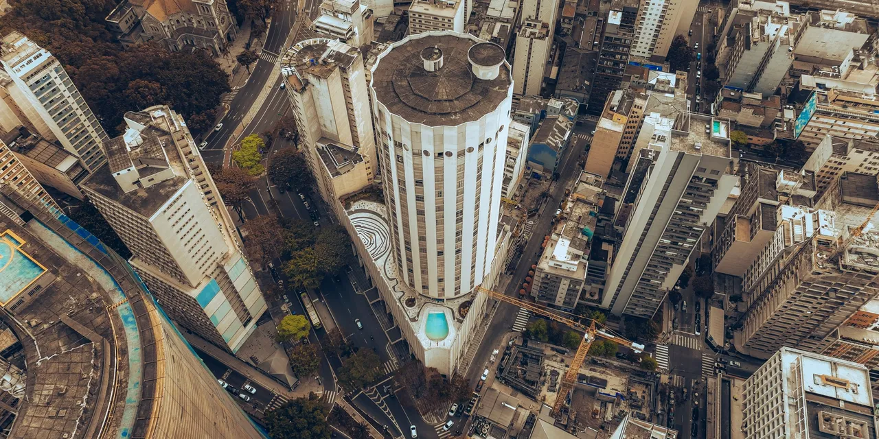 A high aerial view over dense central São Paulo, with a cylindrical tower among packed high-rise blocks.