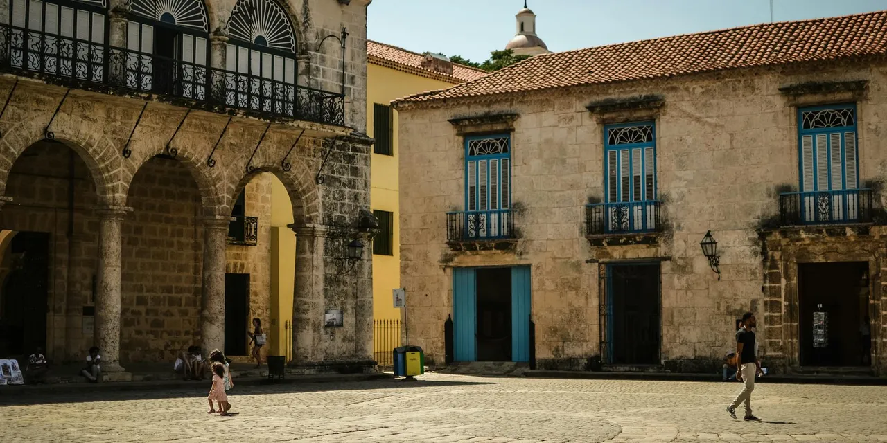 Sunny day in Havana showcasing colonial architecture with people walking through historic streets.