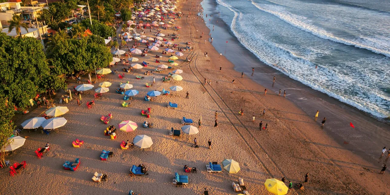 Aerial shot of lively beach with colorful umbrellas and ocean waves in Bali, Indonesia.