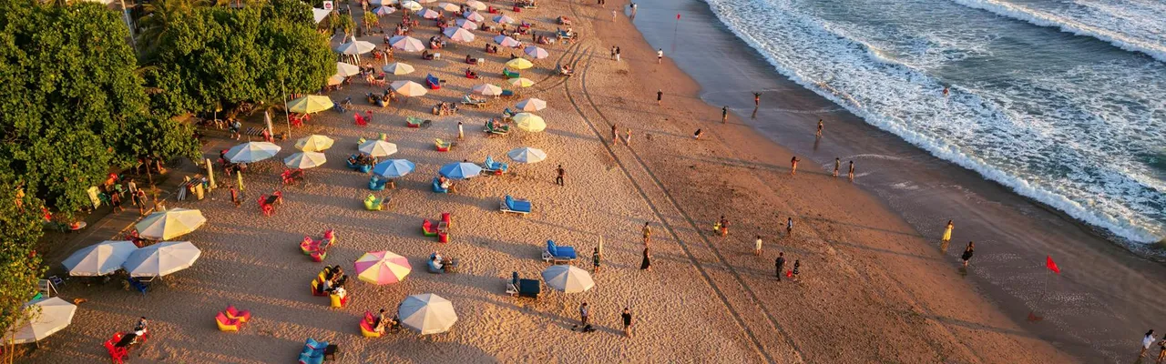 Aerial shot of lively beach with colorful umbrellas and ocean waves in Bali, Indonesia.
