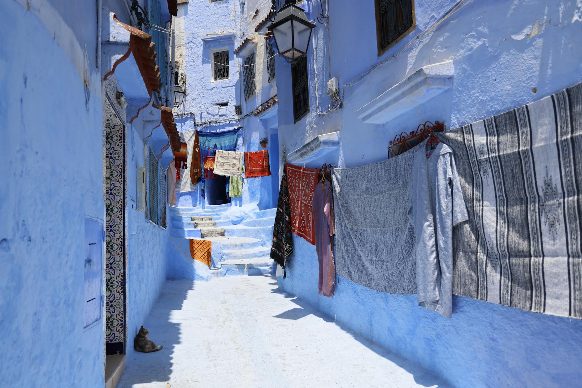 Vivid blue alleyway in Chefchaouen, Morocco with colorful drying clothes, vibrant architecture, and sunny ambiance.