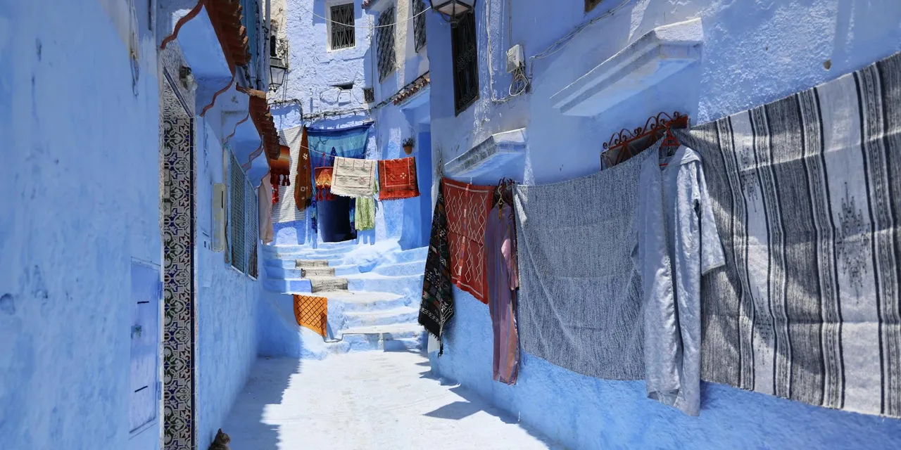 Vivid blue alleyway in Chefchaouen, Morocco with colorful drying clothes, vibrant architecture, and sunny ambiance.