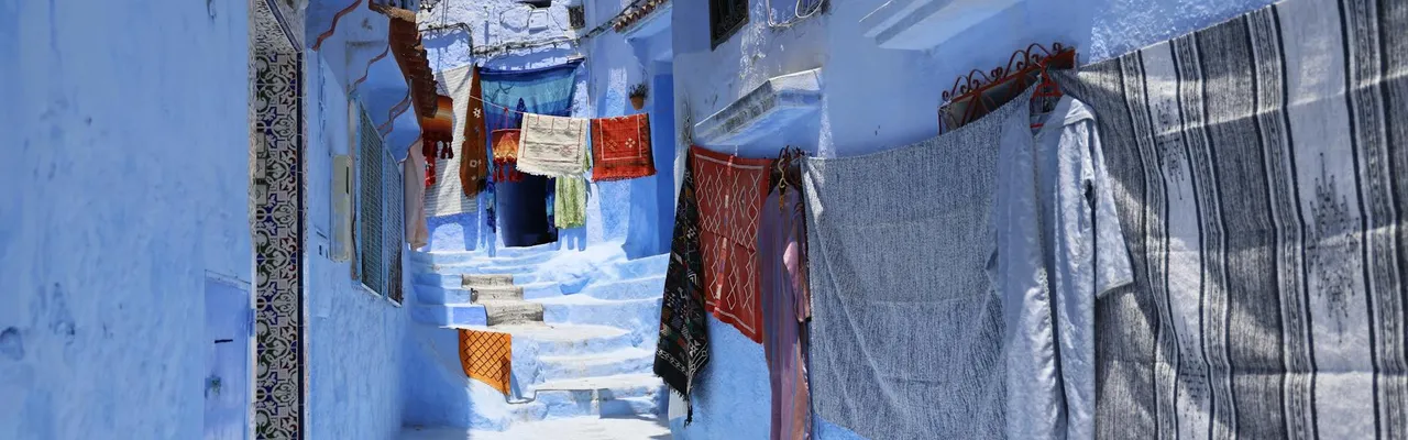 Vivid blue alleyway in Chefchaouen, Morocco with colorful drying clothes, vibrant architecture, and sunny ambiance.