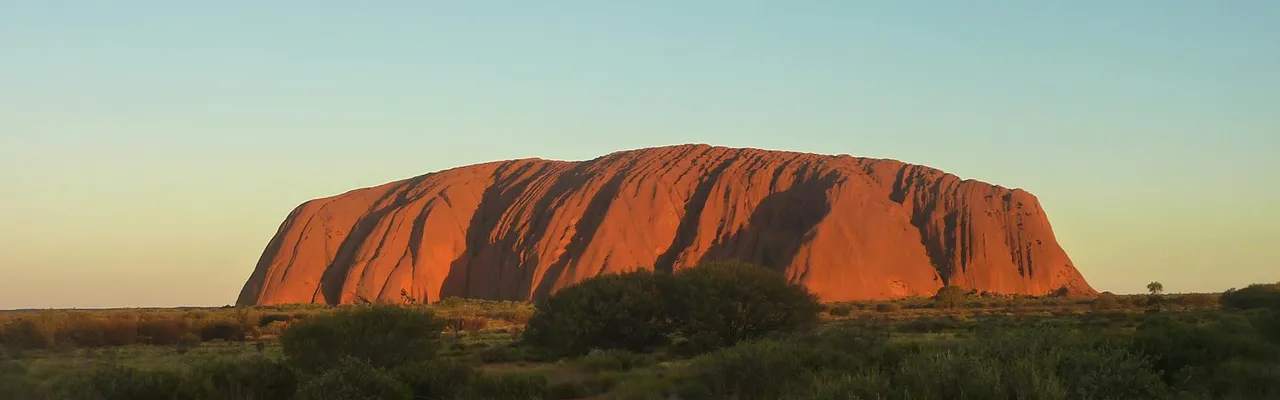 Capture the majestic Uluru rock formation glowing under the sunset. A natural wonder in Australia's Outback.