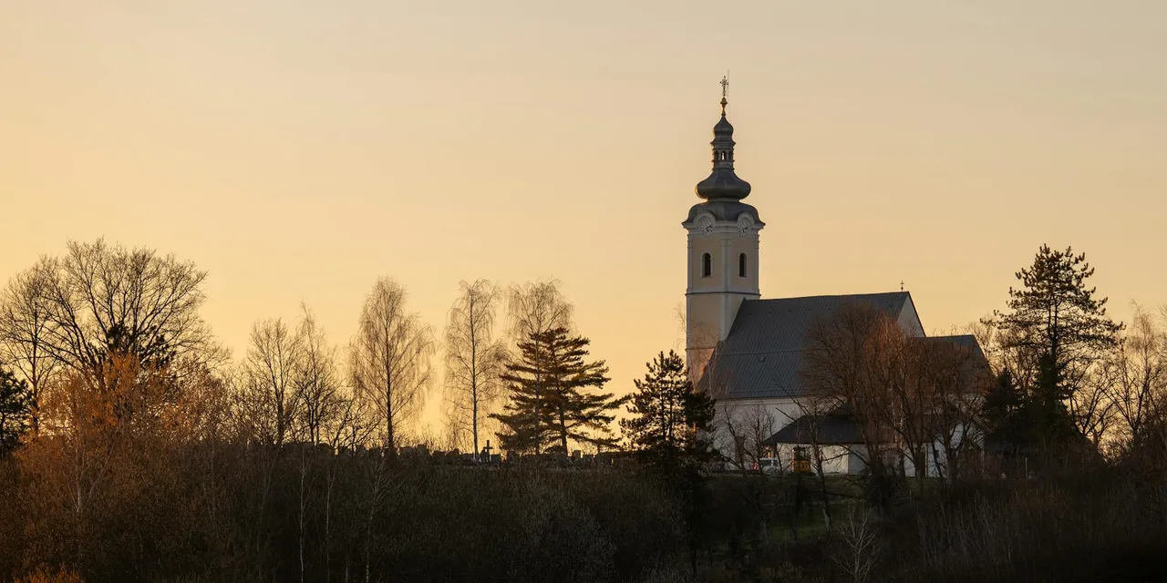 A picturesque church in Garešnica, Croatia, surrounded by autumn trees during sunset.