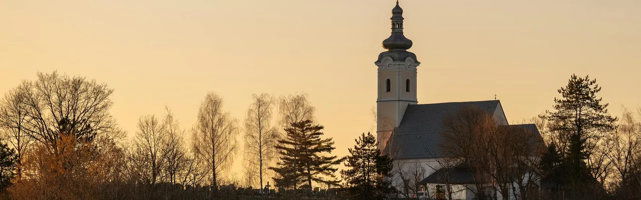 A picturesque church in Garešnica, Croatia, surrounded by autumn trees during sunset.