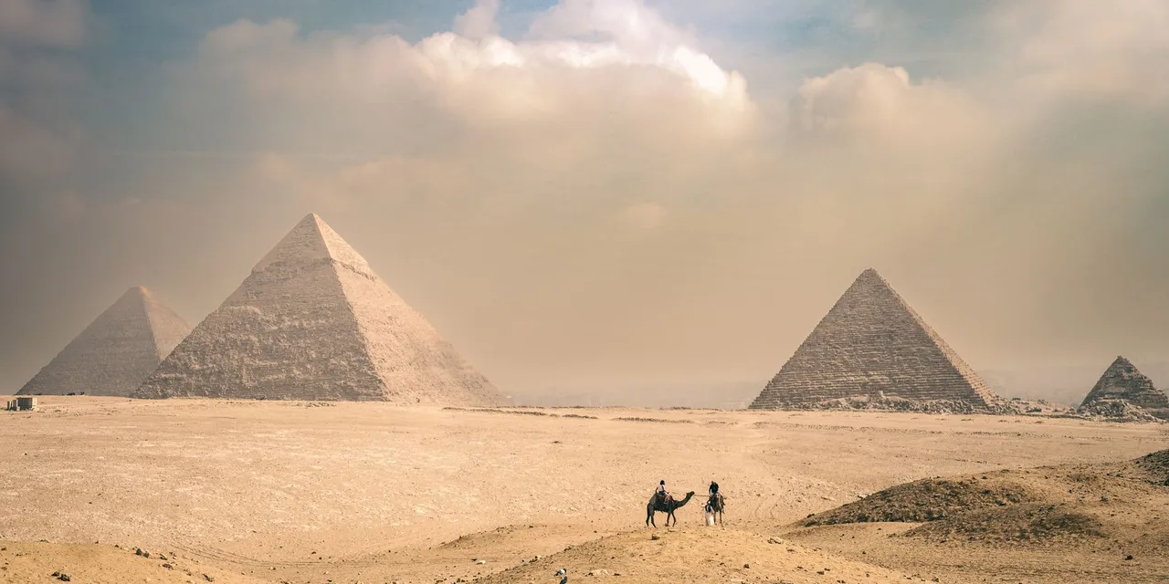 Explore the majestic Pyramids of Giza under a sunny sky with distant travelers on camels.