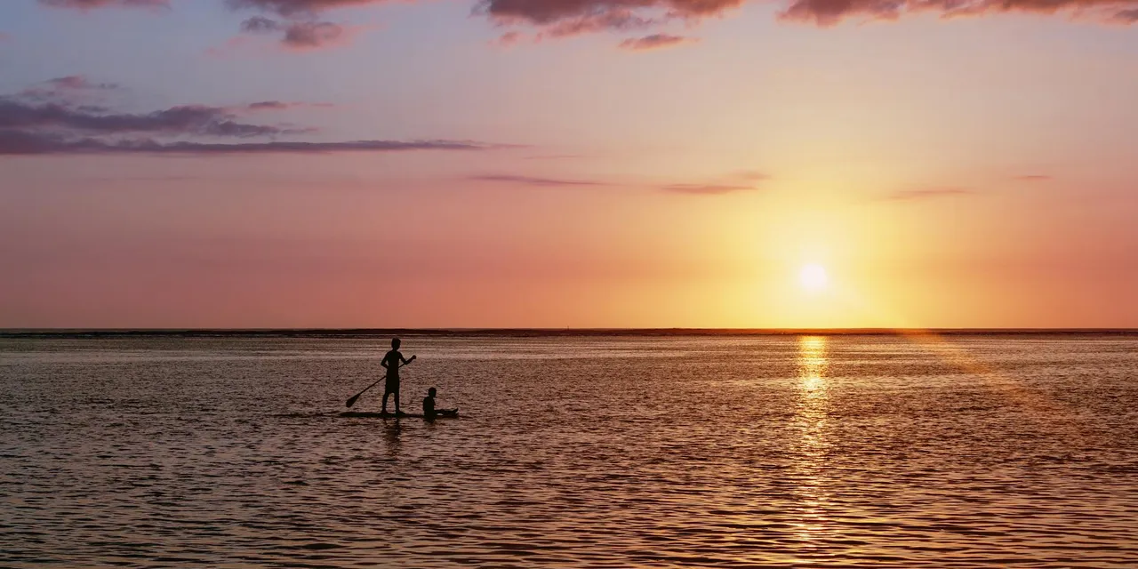 A vibrant sunset over the ocean with silhouettes of paddleboarders on Réunion Island.
