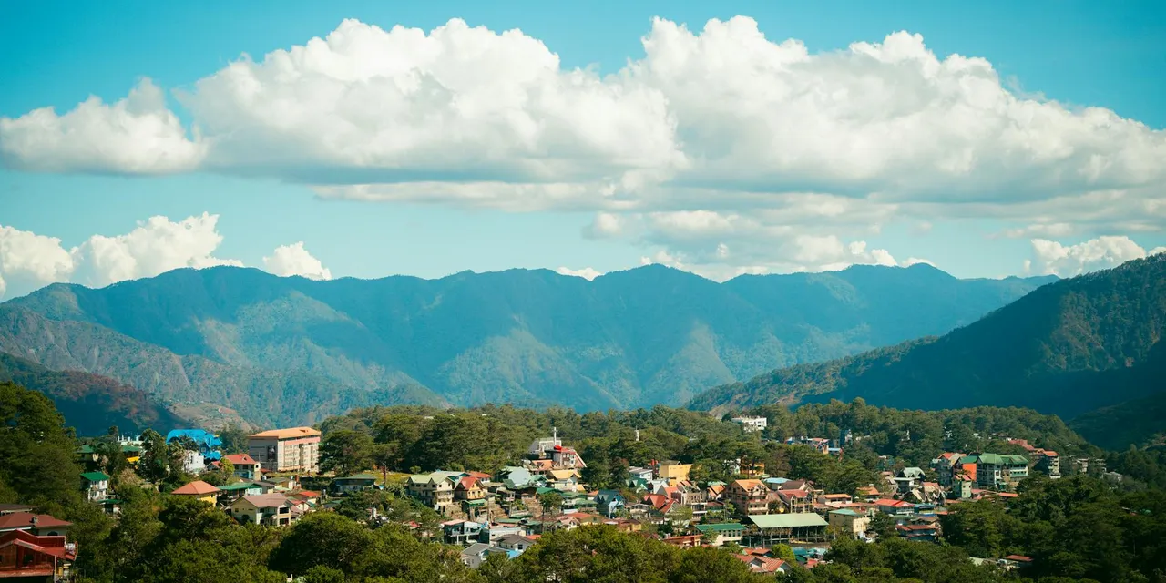 Breathtaking panoramic view of Baguio cityscape against majestic mountain backdrop under blue skies.