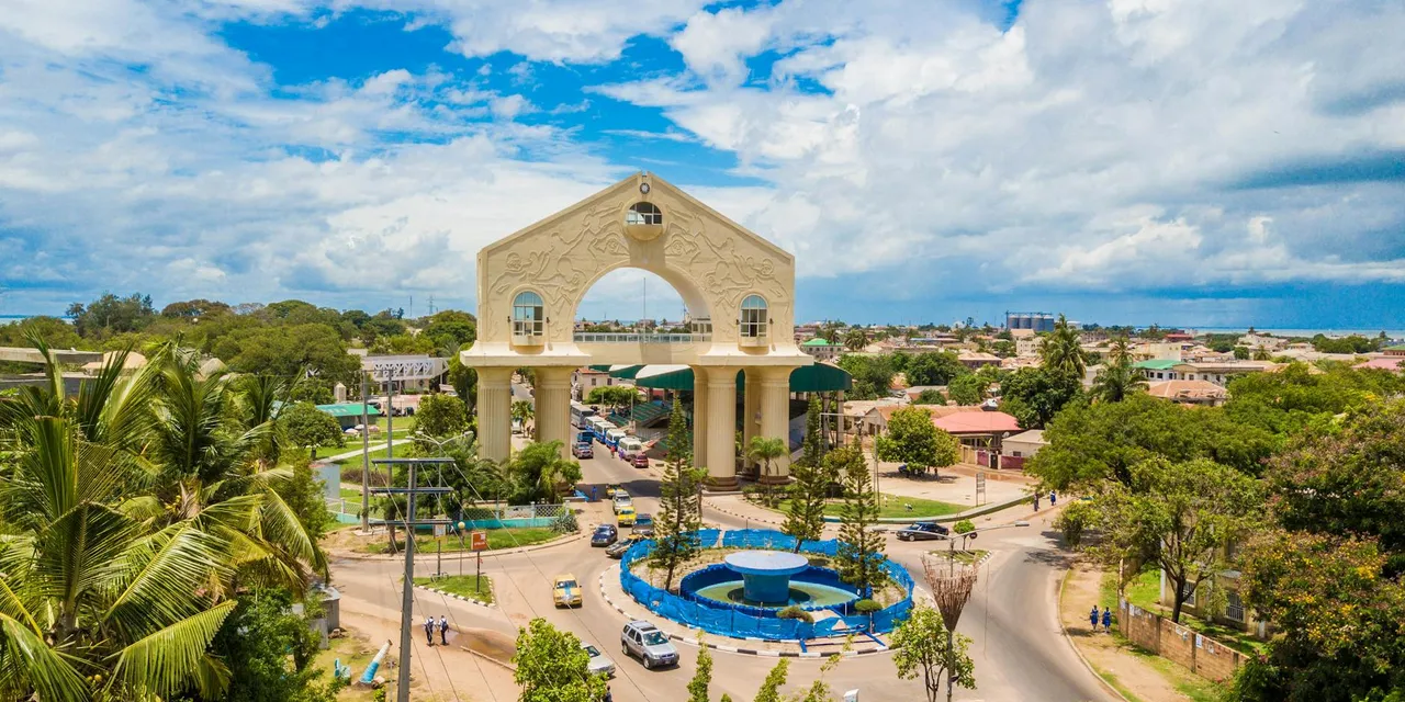 Scenic aerial view of Arch 22 in Banjul, The Gambia amid lush greenery and cloudy sky.