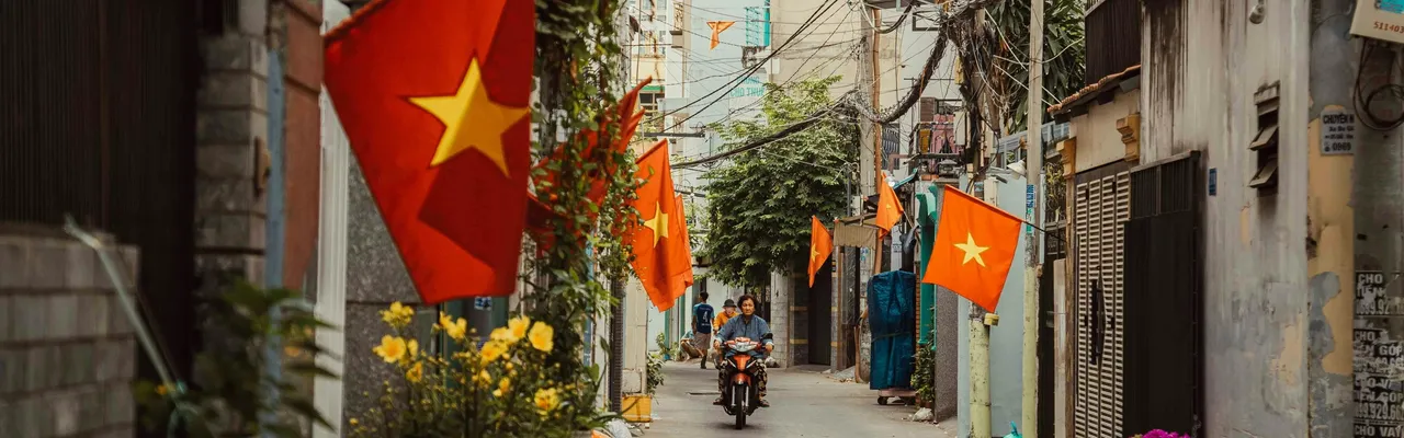 Vietnamese flags lining a narrow alley with a motorbike rider, Vietnam