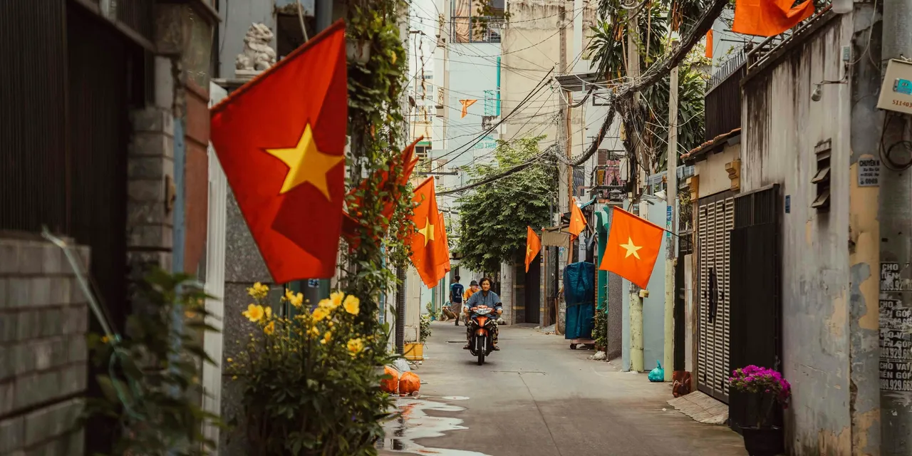 Vietnamese flags lining a narrow alley with a motorbike rider, Vietnam