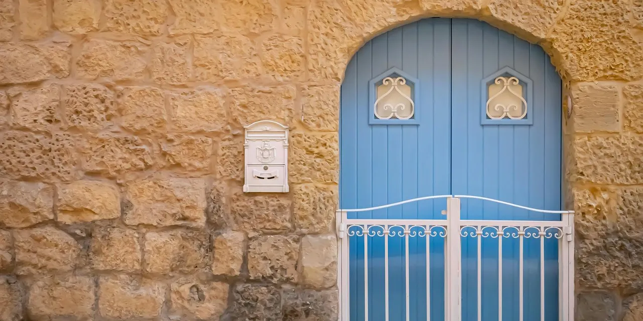 A picturesque blue arched door set in a traditional stone facade in Malta's historic streets.