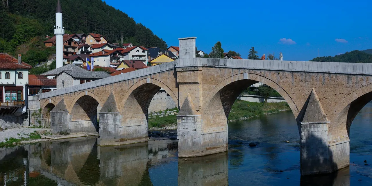 A stunning stone bridge with reflections in a tranquil river under a clear blue sky in Kosovo.