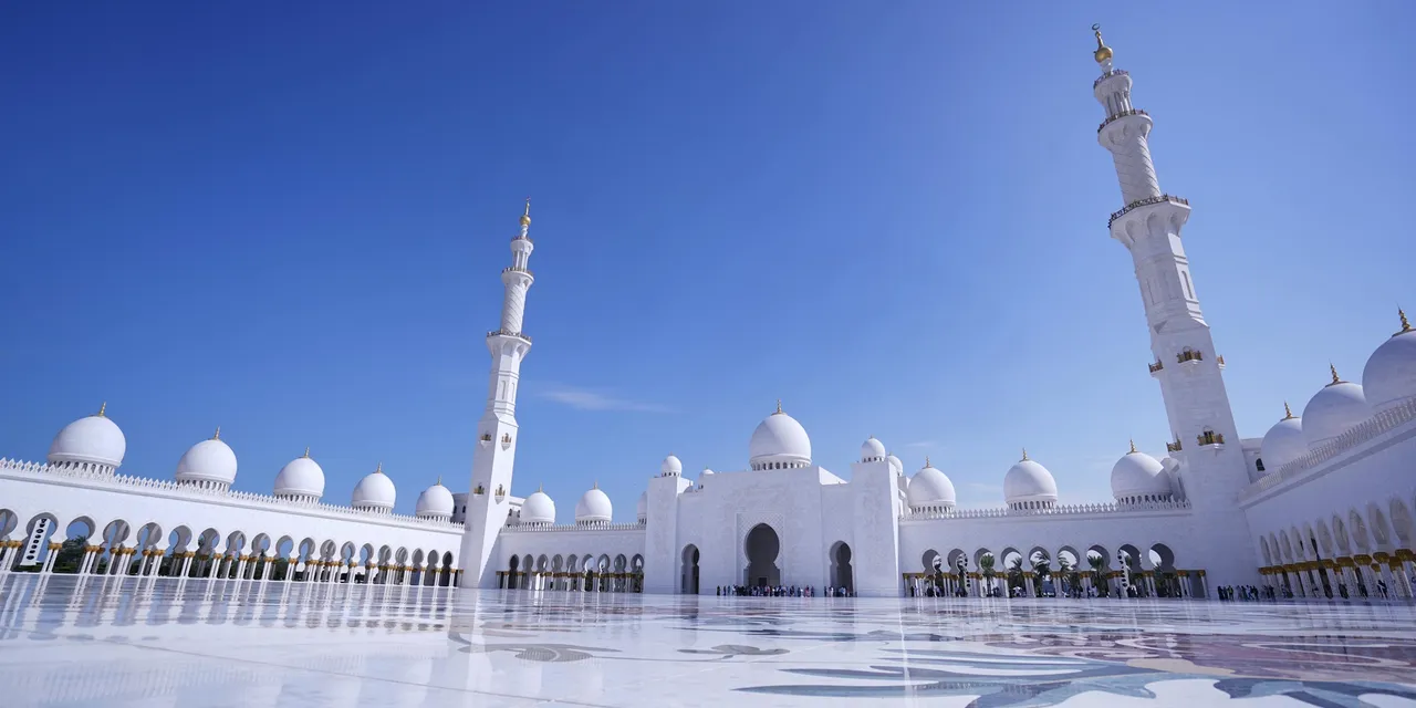 Sheikh Zayed Grand Mosque gleaming white courtyard under blue sky, Abu Dhabi, UAE