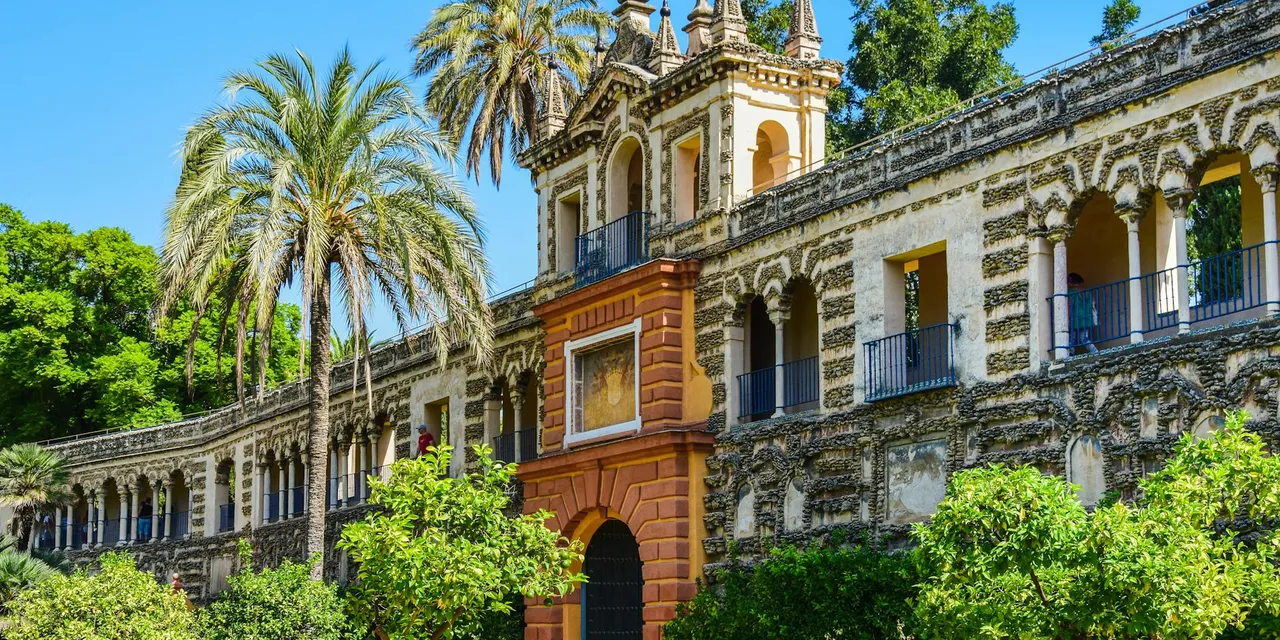 Discover the stunning Alcazar Palace with lush gardens, palm trees, and historic architecture in Seville, Spain.