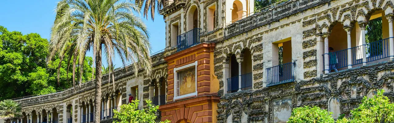Discover the stunning Alcazar Palace with lush gardens, palm trees, and historic architecture in Seville, Spain.